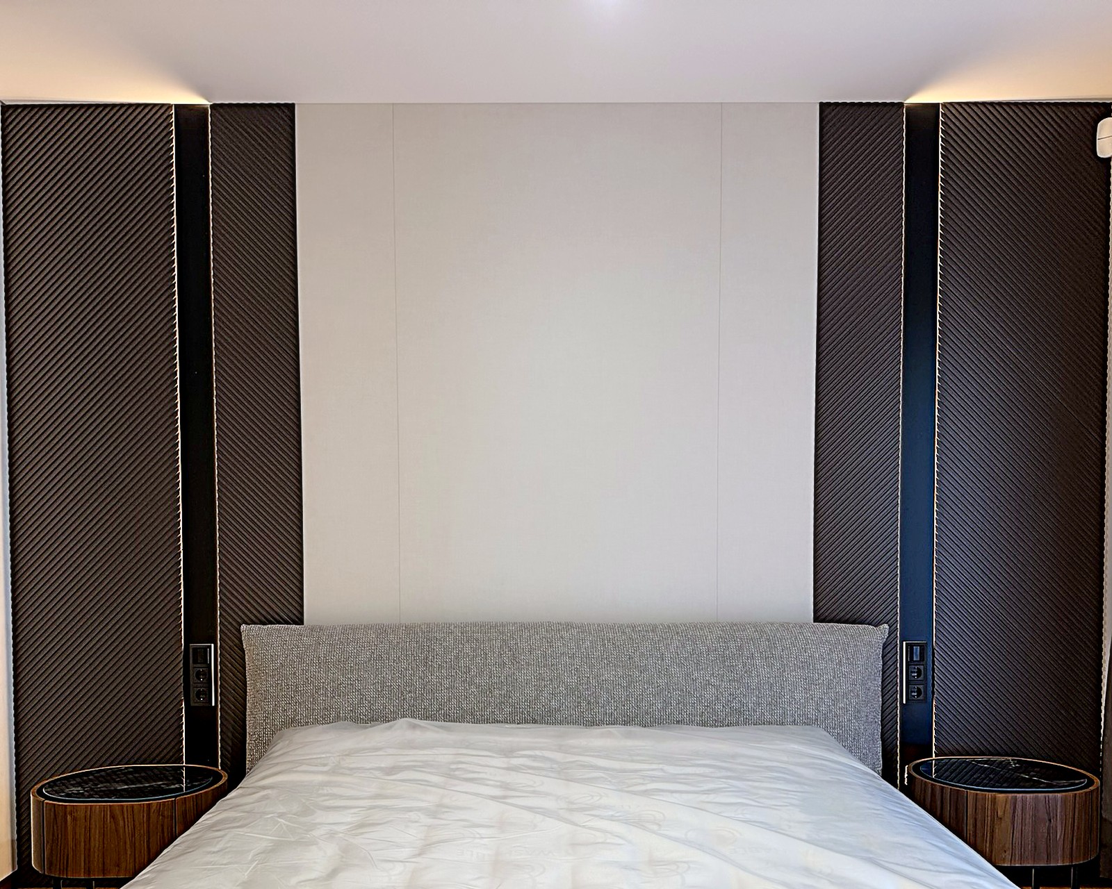 Wandpaneele nach Maß hinter dem Bett mit strukturierten Flächen und Lichtfugen
